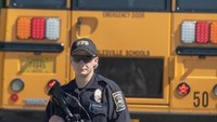 Polisi bersenjata menjaga bus sekolah yang dipakai untuk mengevakuasi para siswa SMP Noblesville West ke SMA terdekat. Foto: Kevin Moloney/AFP