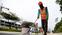 Seorang pekerja melakukan pengecatan trotoar.