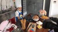 Chef El Barack siap beraksi nih. Ia sudah duduk manis di depan meja berisi bahan baku untuk membuat kue. Pakaiannya juga sudah mirip chef yang lengkap dengan topi koki. Foto: instagram @alexanderbarackel