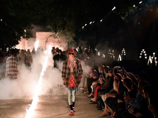 Para model berjalan di halaman Promenade Des Alyscamps ditemani obor dan lilin gereja. Suasana pun kian terasa mistis berkat perapian panjang yang membelah catwalk tersebut. (Foto: AFP PHOTO / BERTRAND LANGLOIS)