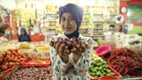 Pedagangan memperlihatkan bawang merah di depan kamera.