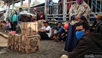 Pemudik menunggu bus di samping tumpukan barang bawaan.