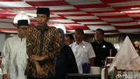 Dia tampak mengenakan peci berwarna hitam dengan baju batik cokelat serta celana hitam.