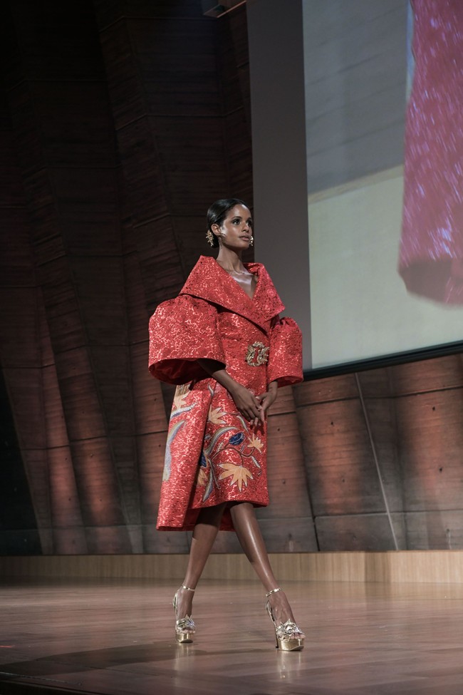 Sukses mencuri atensi, look pertama yang menampilkan gaun merah bersiluet coat dengan kerah dan lengan bervolume. Busana ini hadir dengan motif batik yang Denny tempel di atas bahan jacquard berkilauan dengan teknik bordir. Foto: Rio Motret/Image Dynamics