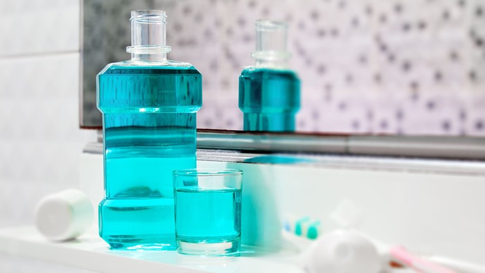 Oral cleanser for good oral health, Bottle and glass of mouthwash on bath shelf with blurred toothbrush and toothpaste in foreground
