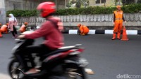 Pemotor melintas saat petugas PPSU melakukan pengecatab trotoar.