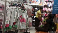 Seorang anak tertidur di gendongan ayahnya, sementara ibu memilih barang.
