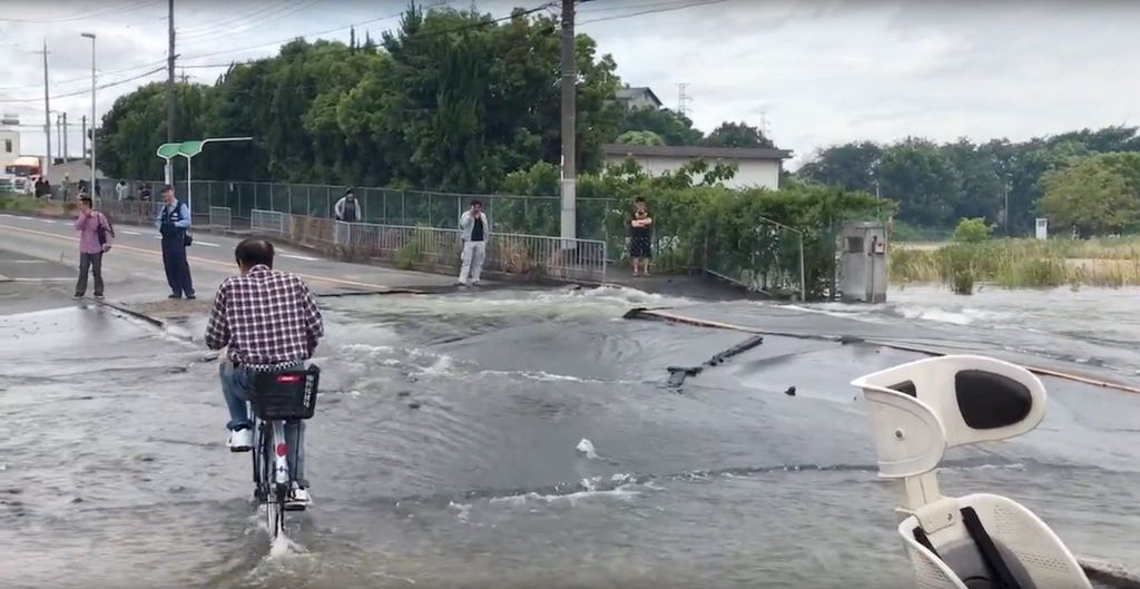 A man cycles on a flooded road damaged after an earthquake hit Osaka, Japan June 18, 2018, in this still image taken from a video obtained from social media. MANDATORY CREDIT.  Twitter/@tw_hds/via REUTERS THIS IMAGE HAS BEEN SUPPLIED BY A THIRD PARTY. NO RESALES. NO ARCHIVES MANDATORY CREDIT.