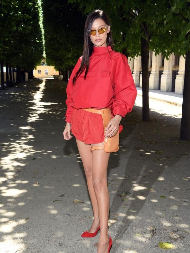 Model Bella Hadid memilih gaun bergaya athleisure merah dengan siluet bervolume yang dipadu dengan heels berwarna senada. Sebagai pelengkap gayanya, adik Gigi Hadid itu mengandalkan tas pinggang yang menyerupai sarung pistol. (Foto: Getty Images)