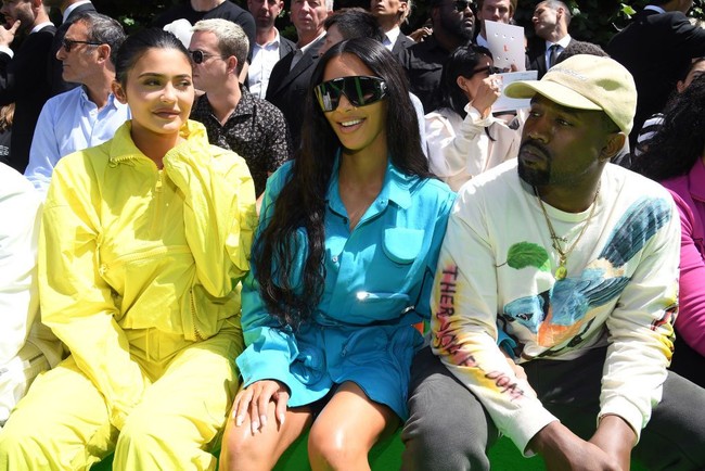 Kim duduk di samping Kylie Jenner yang memakai tracksuit kuning terang dan sepatu berbahan PVC. Hadir pula rapper Travis Scott, kekasih Kylie yang juga ayah dari putrinya, Stormi Webster. Foto: Dok. Getty Images