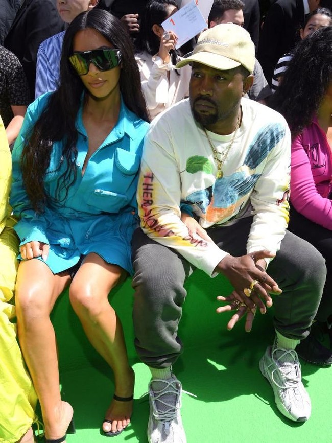 Shirt dress biru tosca menjadi pilihan Kim Kardashian. Tak tampak perhiasan berkilauan yang menemani gayanya. Sepertinya Kim masih trauma dari perampokan yang dialaminya di Paris dua tahun lalu. Sementara itu sang suaminya, Kanye West, tampil kasual dengan sweater bermotif burung, sweatpants abu-abu, dan ugly sneakers. (Foto: Getty Images)
