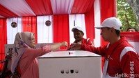 Petugas membantu warga memasukkan kertas suara ke kotak suara.
