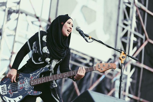 Gitaris cantik itu tampil memakai hijab instan berbentuk hoodie. Hijab berwarna hitam dan berbahan kaos itu ia padukan dengan scarf bermotif tengkorak di bahunya. Foto: Instagram/ChuaKotak
