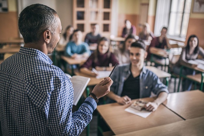 Rear view of male professor teaching high school students in the classroom.