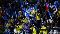 Penonton memberikan dukungan sambil menepukkan balon.