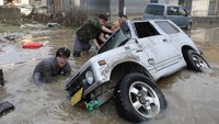 Tampak warga lokal Okayama bergotong-royong untuk menegakkan sebuah mobil yang terguling akibat banjir yang menerjang. Foto: AFP PHOTO/JIJI PRESS