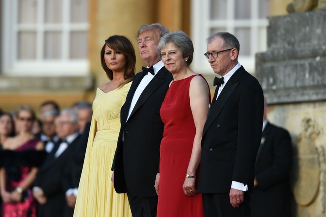 Theresa May pun menganggap serius dresscode di hari itu. Ia tampil anggun berbalut gaun sleeveless merah, sementara suaminya memakai tuksedo klasik seperti Donald Trump. Foto: Getty Images