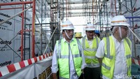 Budi karya berkeliling Stasiun Kelapa Gading Boulevard dengan mengenakan rompi dan helm proyek.