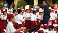 Seorang guru sedang mengatur barisan anak-anak untuk melakukan upacara di lapangan sekolah.