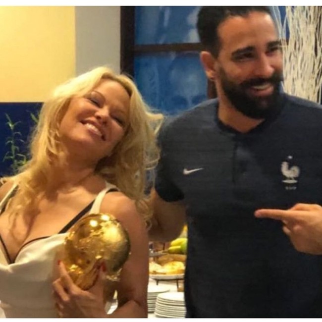 Dalam sebuah foto yang beredar di media sosial, tampak Pamela Anderson ikut memegang trofi Piala Dunia dengan Adil Rami berada di sampingnya. Rumor pertunangan pun merebak karena foto itu. Foto: Instagram/@teamfrenchwags