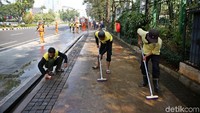 Tiga orang petugas menyikat kotoran yang menempel di atas trotoar.