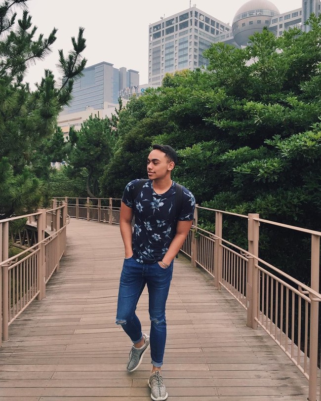 Bersantai di sebuah taman, pria beralis tebal ini mengandalkan kaus gelap ketat bermotif floral yang mempertegas torso kekarnya. Lalu jeans beraksen sobek dan sneakers Yeezy dipilih sebagai bawahan. (Foto: Instagram/@rafihaikal123)