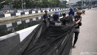 Sejumlah pekerja bersiap untuk memasang waring di atas kali yang warna airnya berwarn hitam pekat.