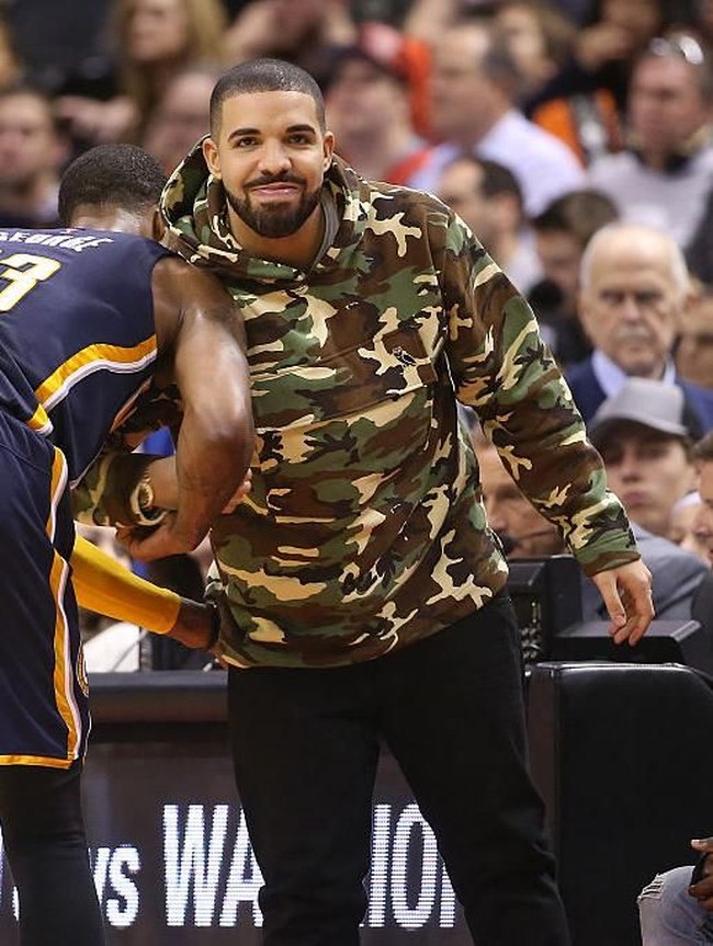 Pria 31 tahun ini juga tak mau melewatkan laga NBA hanya dengan tampil biasa-biasa saja. Hoodie bermotif kamuflase sukses mengangkat gaya Drake. (Foto: Getty Images)