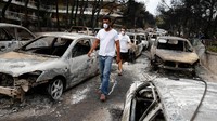 Sejumlah warga Yunani mengenakan masker saat memeriksa puing-puing mobil yang hangus terbakar. Kebakaran ini disebut sebagai salah satu yang terparah dalam abad ini. Foto: REUTERS/Costas Baltas