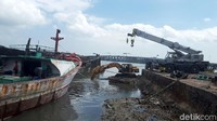 Sejumlah pekerja sibuk menjalankan eskavator untuk membersihkan air di pinggir pelabuhan dari puing-puing kapal yang terbakar.