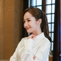 Untuk tampilan yang elegan, Anda bisa memilih kemeja atau blus dengan bahan mengkilap yang lebih tebal. Padukan dengan rok hitam untuk tampilan klasik. Foto: TvN