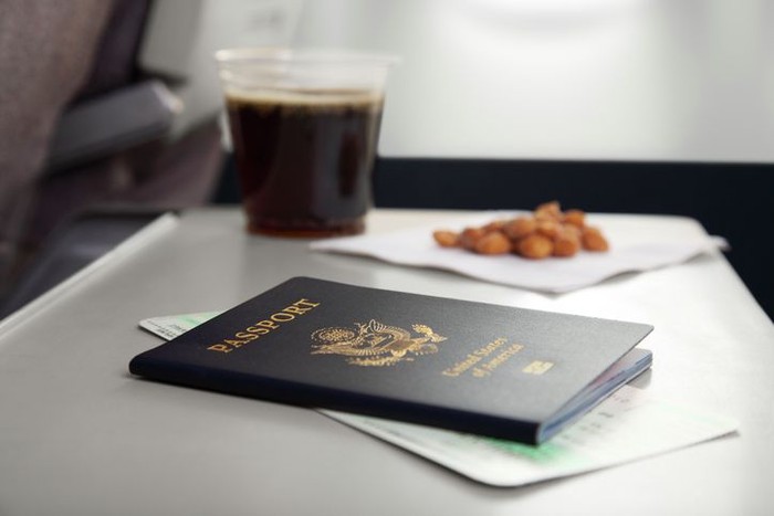 XXXL.  Passport and airplane ticket sitting on a seatback tray table.