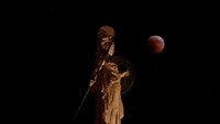 Bulan purnama terbit selama gerhana di belakang patung Dewi Athena kuno di Athena, Yunani, 27 Juli 2018. REUTERS / Costas Baltas