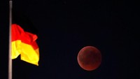 Bulan terlihat saat gerhana bulan di sebelah bendera nasional Jerman di atas gedung Reichstag di Berlin, Jerman, 27 Juli 2018. REUTERS / Fabrizio Bensch