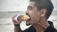 Begini gaya santai Bepe saat makan jagung bakar di tepi pantai, lengkap dengan seragam persija. Foto: Instagram @thenekatchef