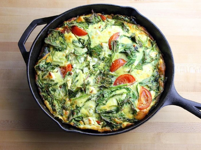 A freshly made spring vegetable frittata in a cast iron pan set on a wooden surface