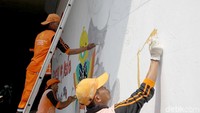 Beberapa orang petugas PPSU sedang melukis gambar maskot Asian Games 2018.