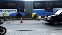 Bus TransJakarta melintas di samping pekerja yang tengah membersihkan pembatas jalur busway.