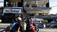 Warga melintas di depan ruko yang hancur akibat gempa, Selasa (7/8). REUTERS/Beawiharta.