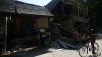 Turis bersepeda di depan bangunan yang roboh.