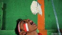 Seorang anak berusaha memakan keruput yang digantung menggunakan tali.