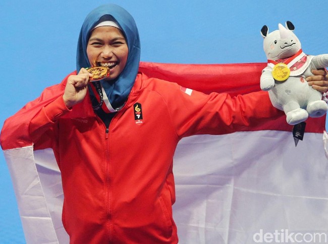 Dengan senyum gembira, atlet taekwondo Defia Rosmaniar menggigit medali emas pertama yang ia persembahkan untuk Indonesia, setelah menang dengan mengalahkan Msarjan Salahshouri dari Iran di babak final poomsae individu putri. Foto: Grandyos Zafna