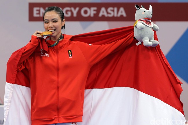 Dari cabang wushu, ada atlet cantik Lindswell Kwok yang menyumbangkan medali emas untuk Indonesia di Asian Games 2018. Dalam balutan jaket merah, Lindswell memasang senyum manis sambil menggigit medali perolehannya. Foto: Agung Pambudhy