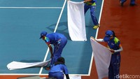 Petugas mengeringkan lapangan tenis dengan handuk.