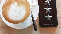 Hot latte dengan latte art jadi teman santai Erico. Di samping segelas kopinya ada juga kacamata hitam dan handphone. Tampaknya Erico ini tergolong millennial yang hobi nongkrong santai. Foto: Instagram @ericomihardja