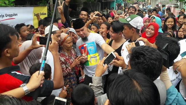 Sebagai anak band, Ahmad Dhani cinta mati pada grup band Queen. Kecintaannya itu pun ditampilkannya pada busananya. Dhani kerap memakai kaus bergambar personel Queen. Salah satunya ketika dia berkampanye di Bekasi. Pentolan Dewa 19 itu memakai kaus abu-abu dengan gambar ilustrasi personel grup band idolanya tersebut. Foto: Dok. Facebook/Instagram Ahmad Dhani