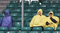 Menggunakan jas hujan, beberapa penonton memioih bertahan di tribun meski suhu dingin menusuk. (AFP PHOTO / Oli SCARFF)