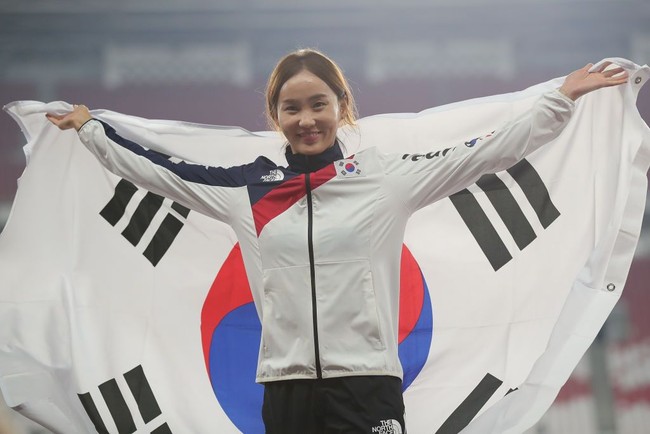 Inilah Jung Hyelim, peraih medali emas untuk cabang lari halang rintang 100 meter di Asian Games 2018. Jung tersenyum bahagia saat membentangkan bendera Korea Selatan di atas podium juara. Foto: Getty Images
