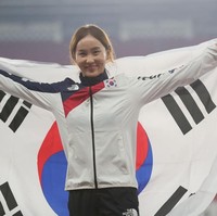 Inilah Jung Hyelim, peraih medali emas untuk cabang lari halang rintang 100 meter di Asian Games 2018. Jung tersenyum bahagia saat membentangkan bendera Korea Selatan di atas podium juara. Foto: Getty Images