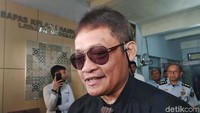Pollycarpus datang dengan mengenakan kemeja hitam serta kacamata.